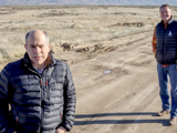 Two gentlemen in black vests on dirt road alongside dry field